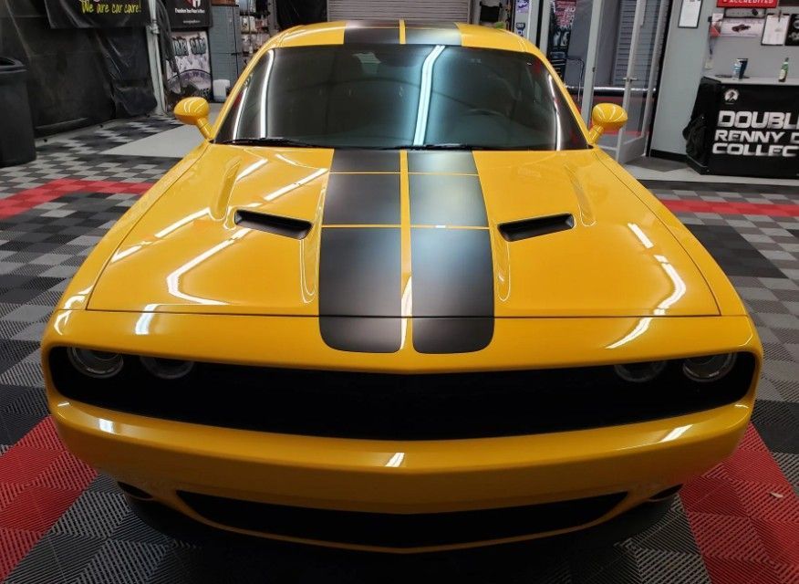 Yellow muscle car with black racing stripes displayed indoors