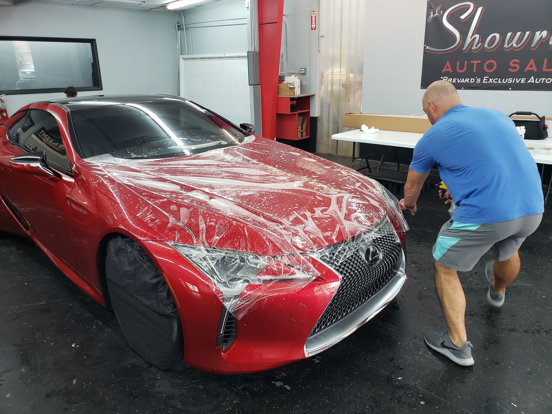 A man is standing next to a red car in a garage.