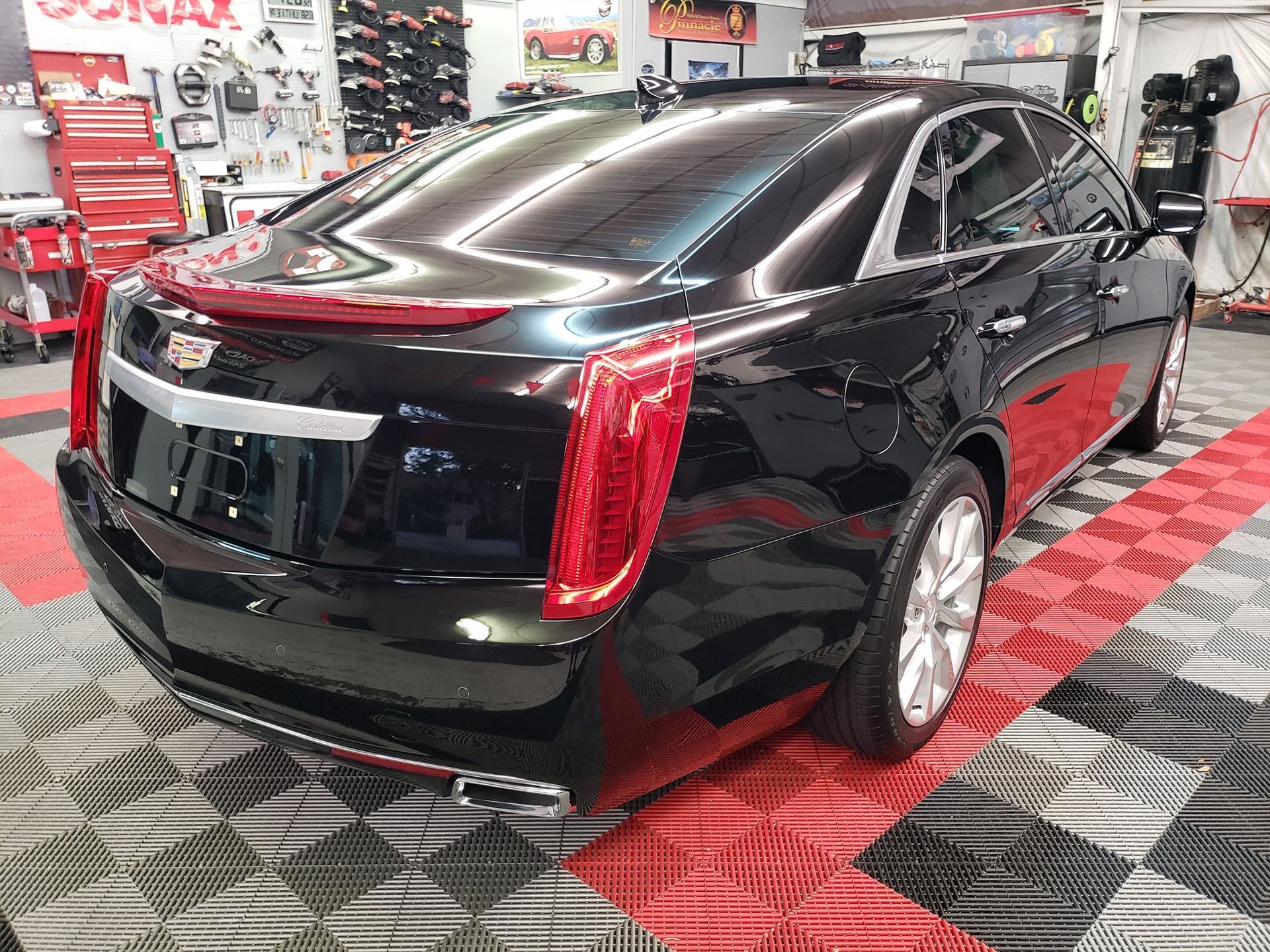 Black Cadillac sedan in an auto shop with red-and-black checkered floor tiles