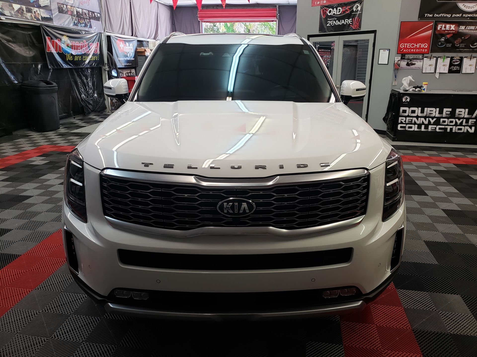 White Kia SUV displayed indoors on a checkered floor in an automotive showroom