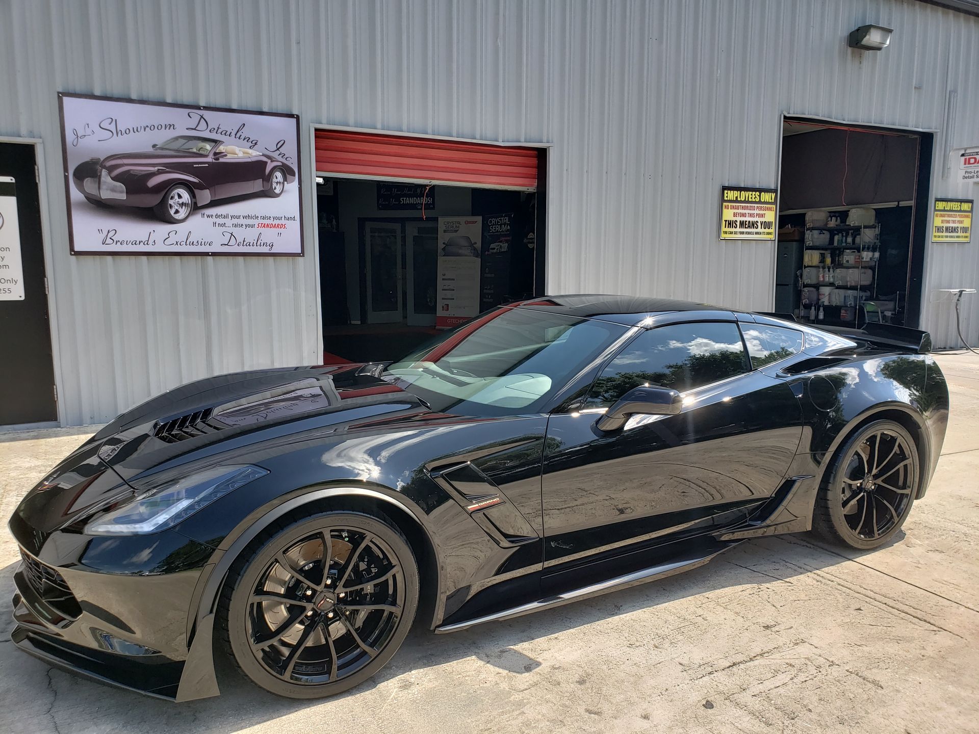 Black sports car parked outside a garage with a Corvette sign above the entrance