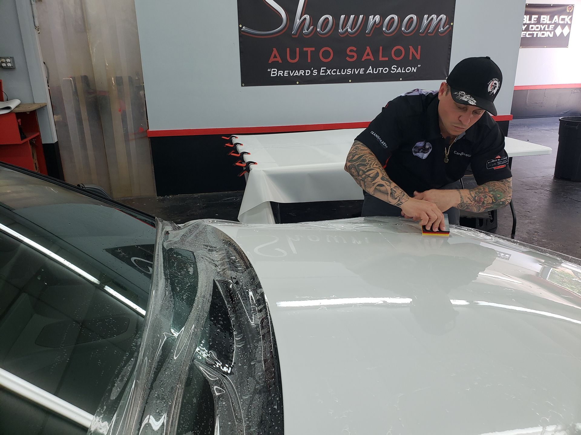 Worker cleaning a white car in an auto salon, with soap suds on the windshield and hood.