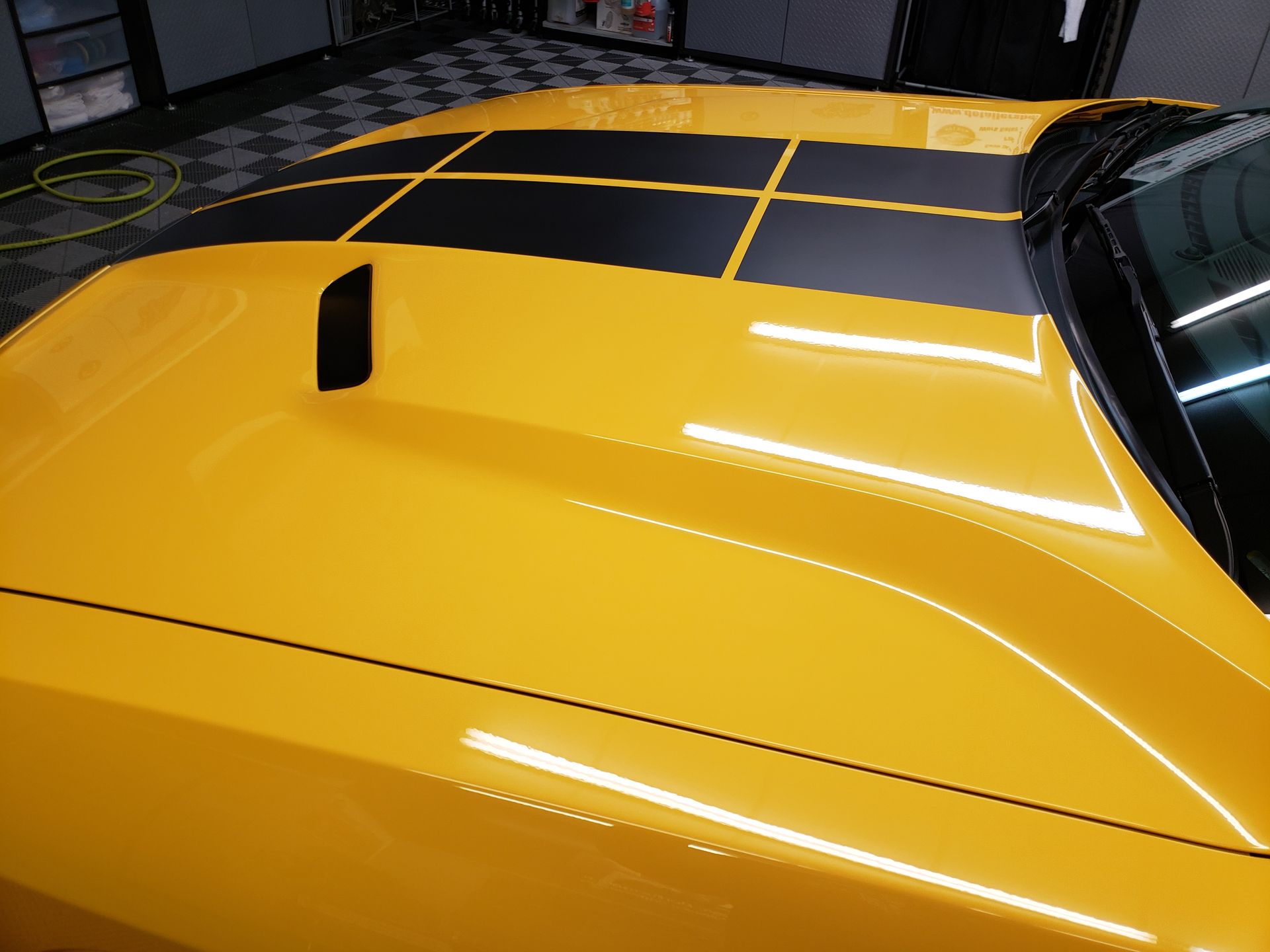 A yellow car with black stripes on the hood is parked in a garage.
