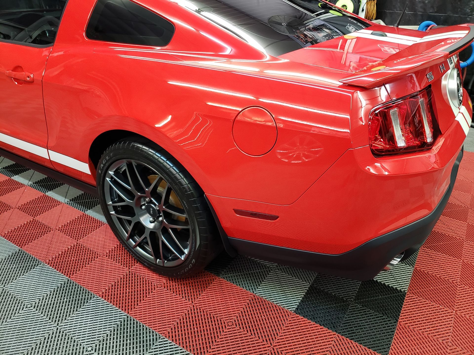 Red sports coupe at an auto show, rear three-quarter view on checkered floor.