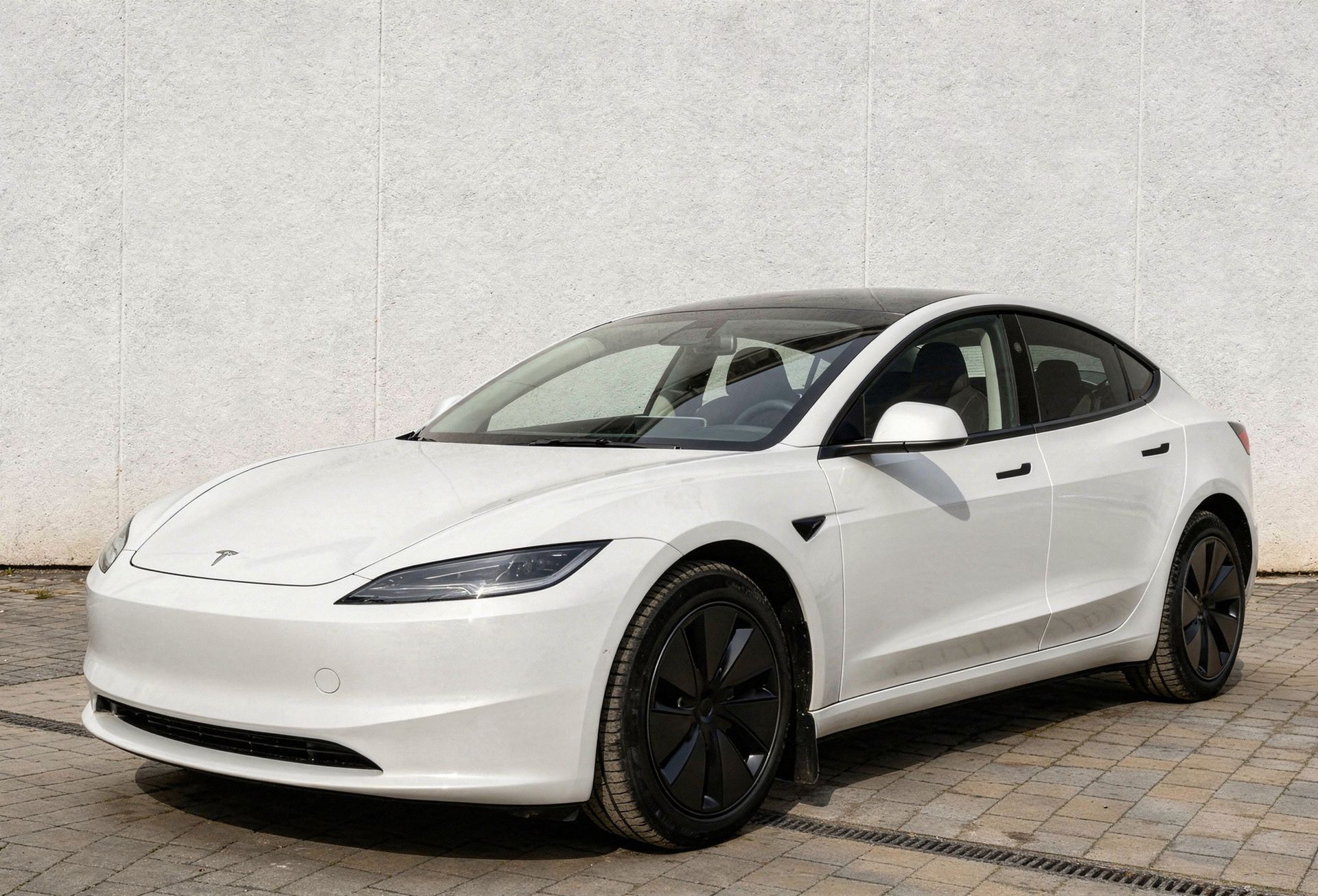 A shiny black Tesla Model S parked inside a brightly lit automotive workshop on a blue lift.