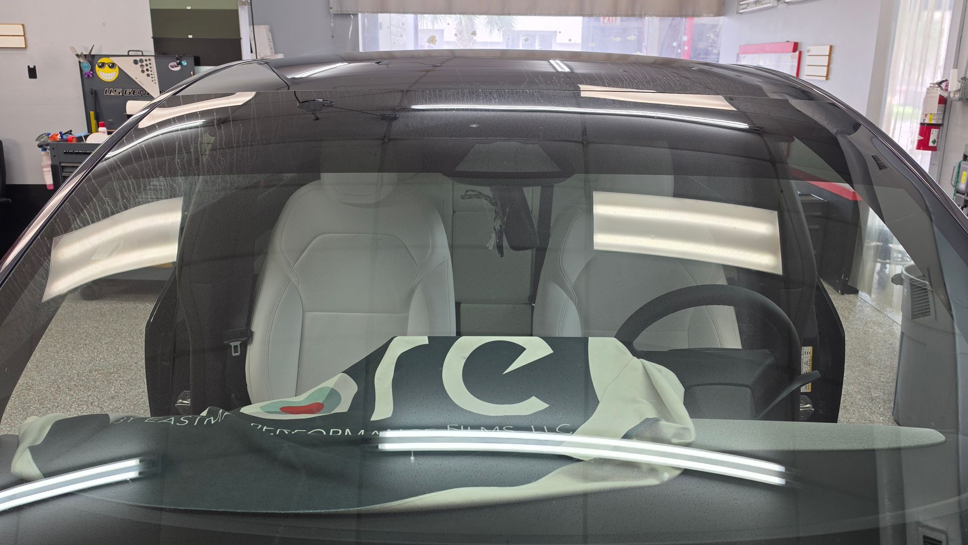 Black car windshield with white marker writing, parked indoors in a garage or service bay