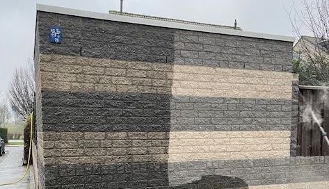 Een bakstenen muur wordt schoongemaakt met een hogedrukreiniger.