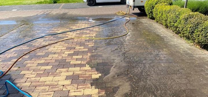 Er wordt een tuinslang gebruikt om een ​​oprit van bakstenen schoon te maken.