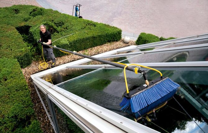 Een man maakt het dak van een gebouw schoon met een borstel.