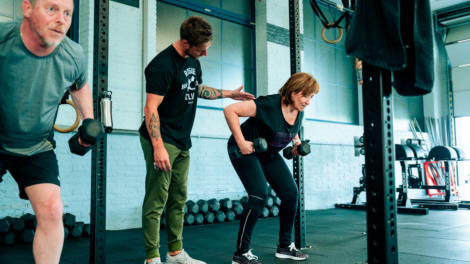 Twee mensen trainen met een trainer in een sportschool en doen een squat met dumbbells.