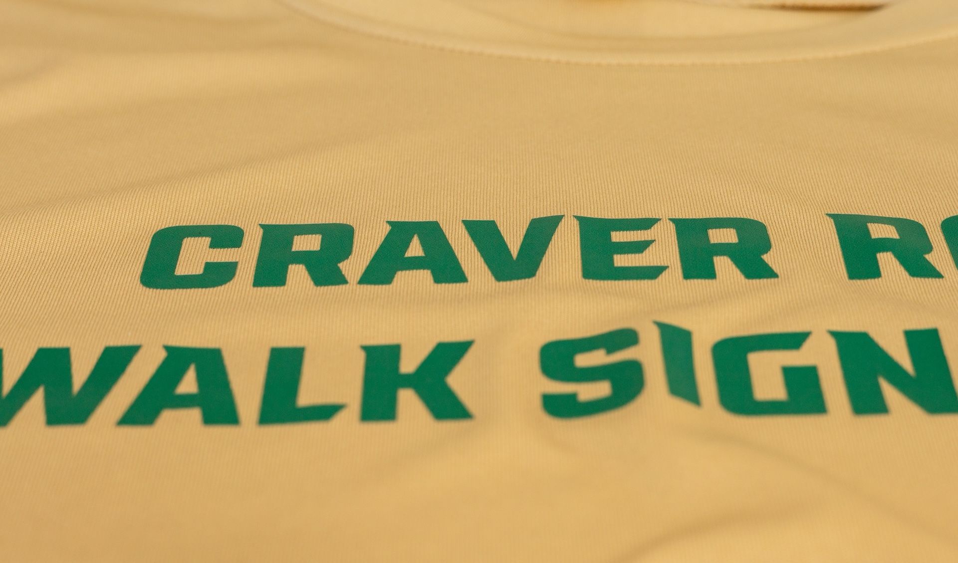 Green text on yellow sand reading “CRAVER R... WALK SIGN”