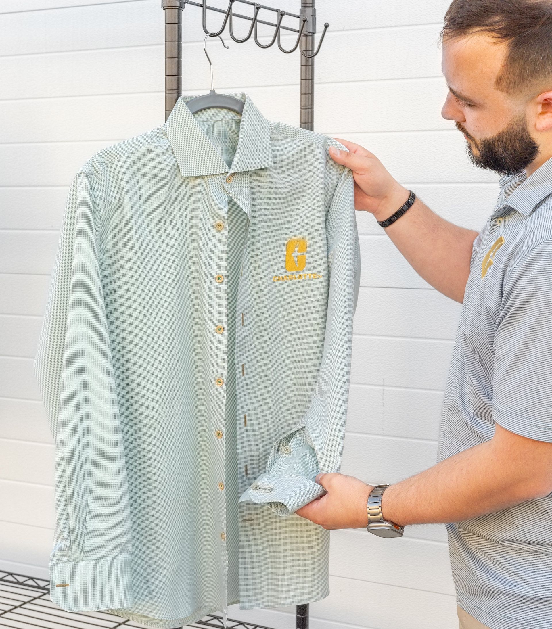 Man examining a light blue striped button-up shirt on a hanger in a bright tiled room