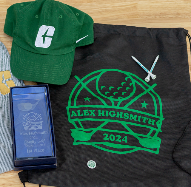 Graduation gift set with green cap, black Alex Highsmith 2024 bag, and blue boxed keepsake on wood surface