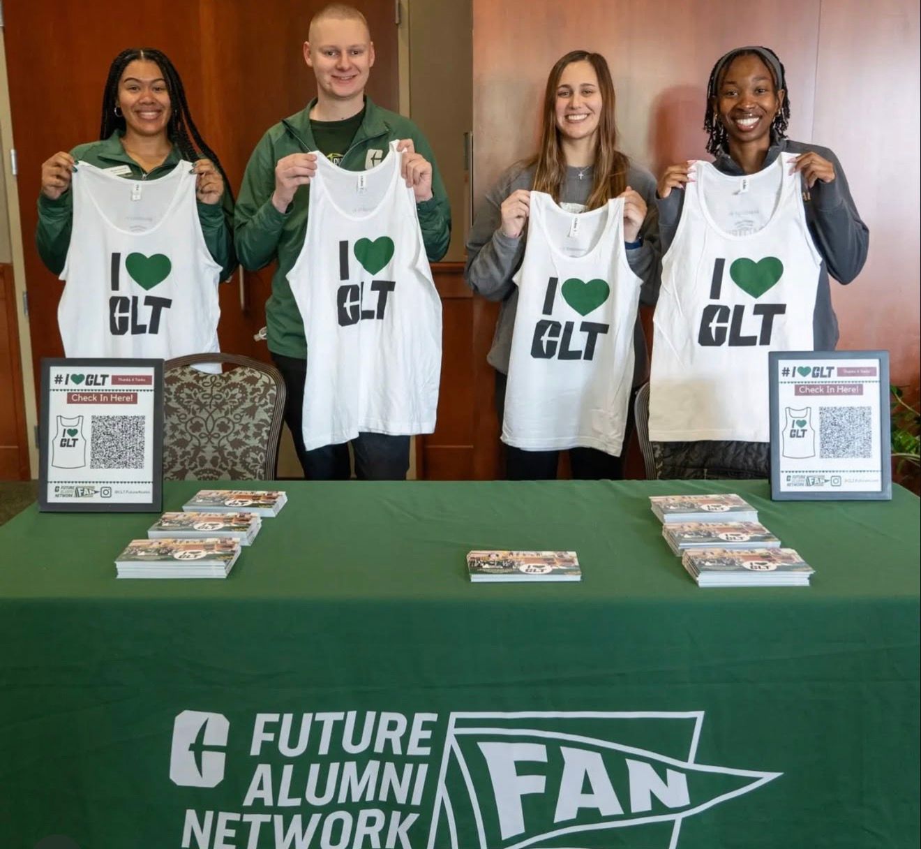 Four people behind a table holding “I ♥ CLT” bags at a Future Alumni Network fan event