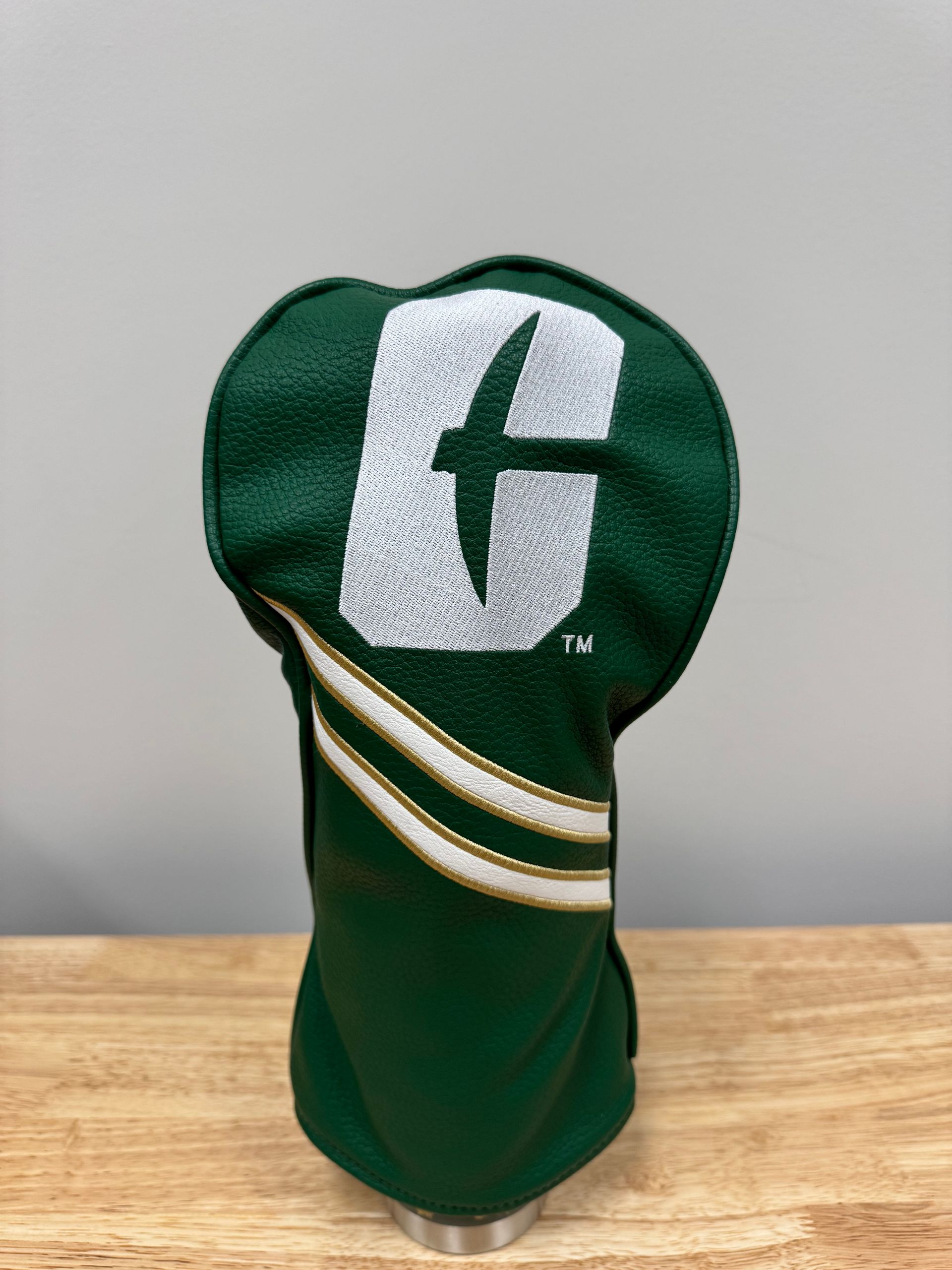 Green embroidered headcover with a white letter C and gold diagonal stripe on a wooden surface