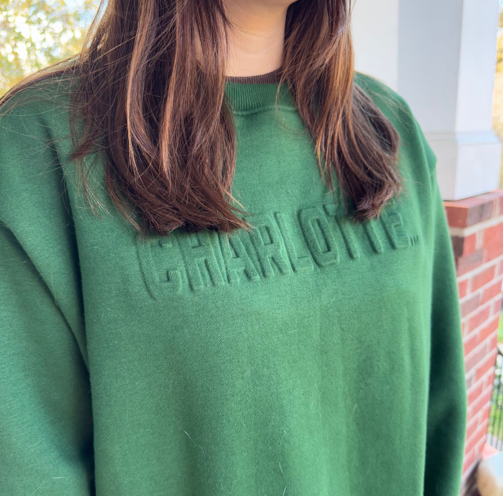 Close-up of a person wearing a green sweatshirt with embossed lettering outdoors