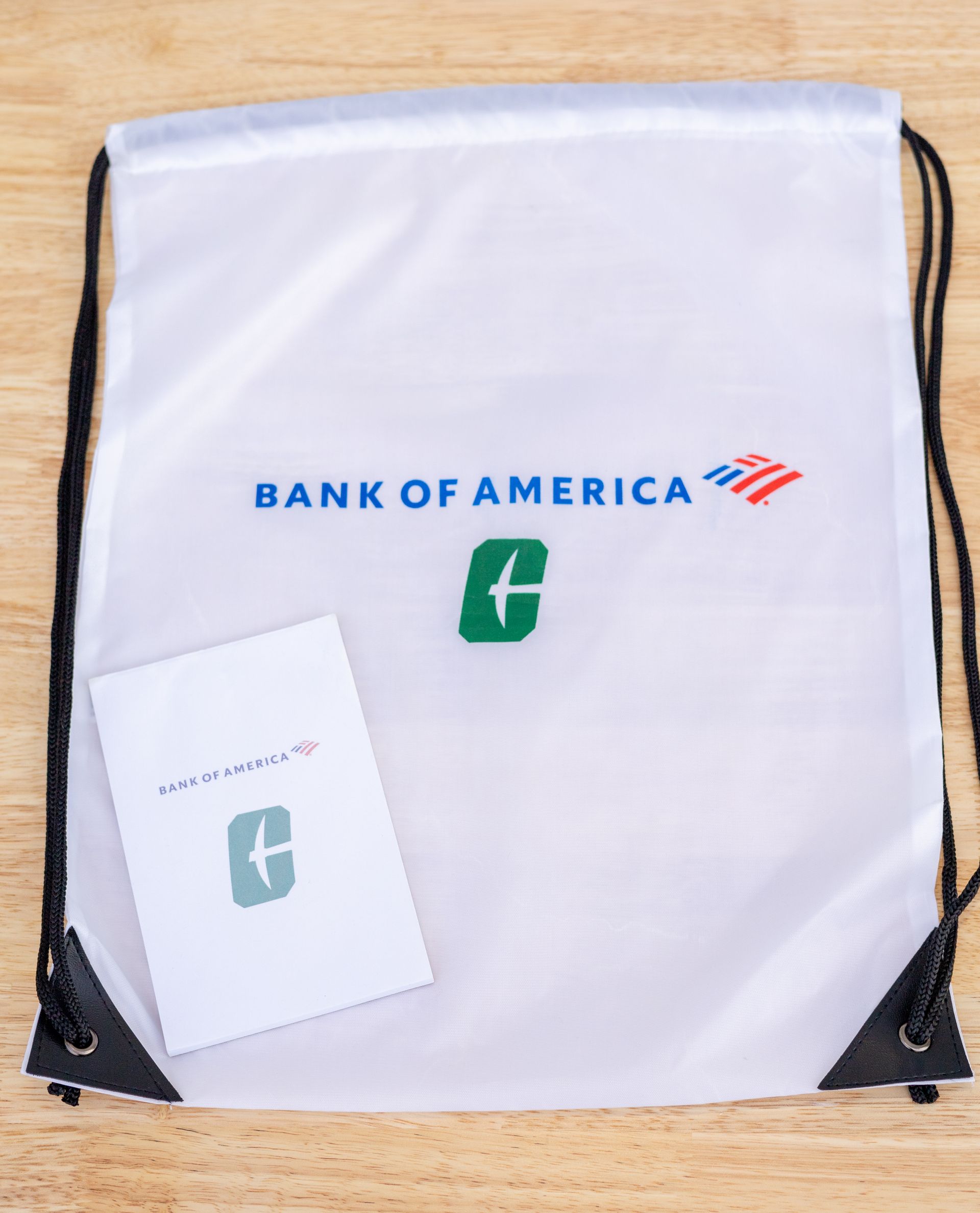 White Bank of America drawstring bag with a green logo and tag on a wooden surface