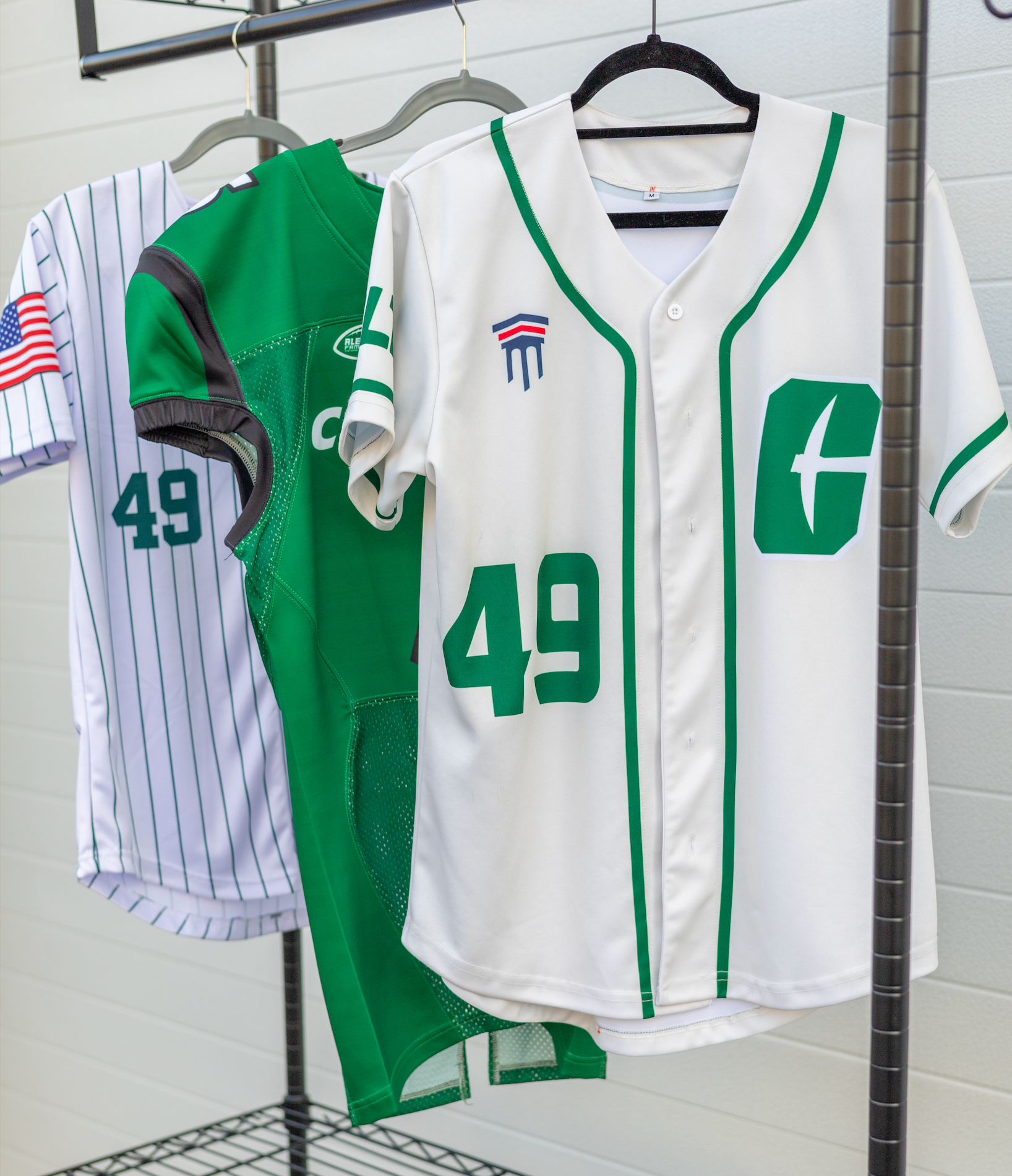 Three hanging baseball jerseys: white with green trim, green, and pinstripe white, each with number 49.