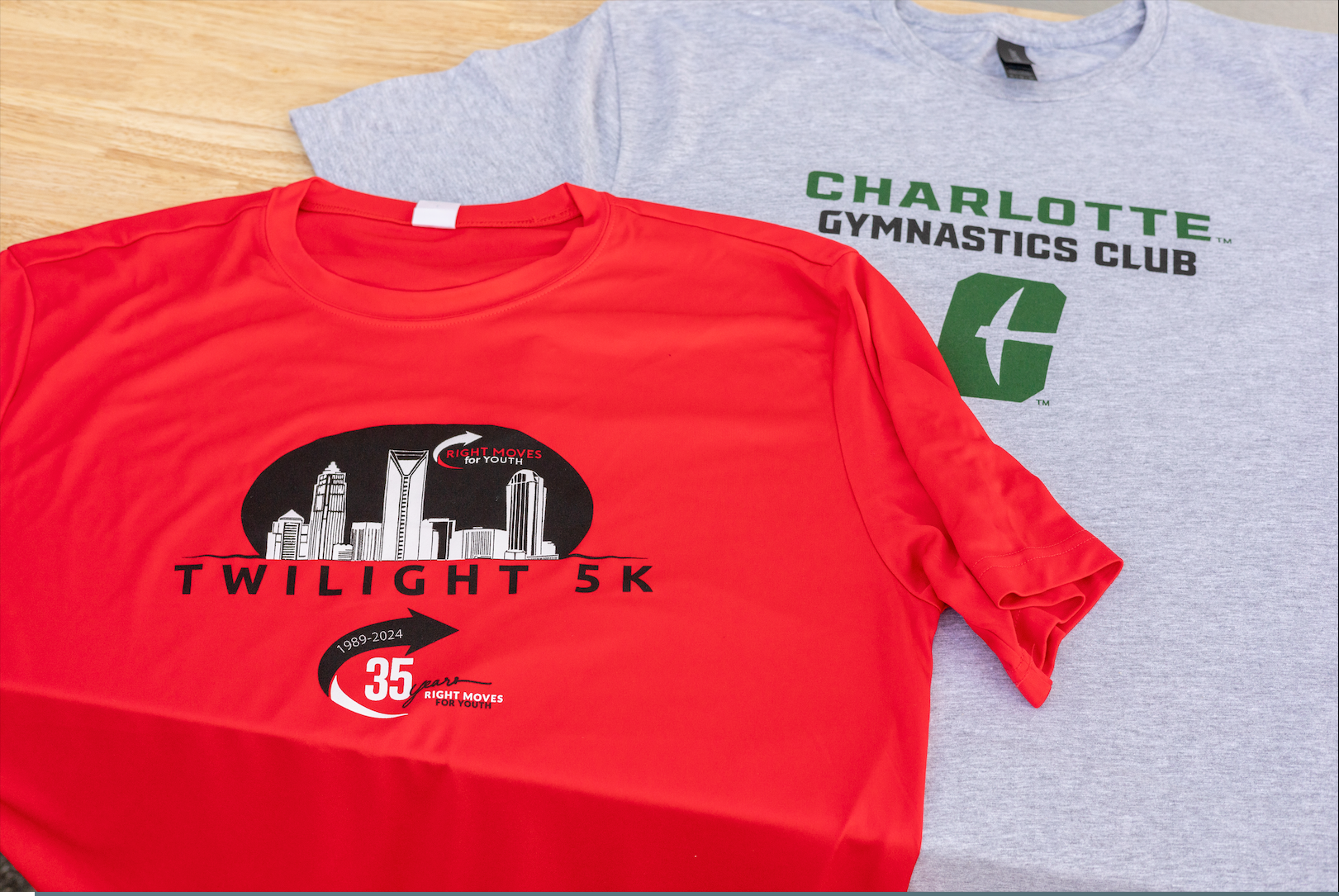 Red and gray Charlotte Gymnastics Club Twilight 5K T-shirts laid on a wooden surface