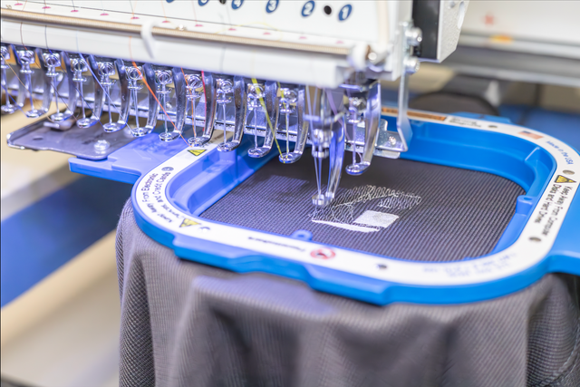 Embroidery machine stitching a blue cap hoop on dark fabric