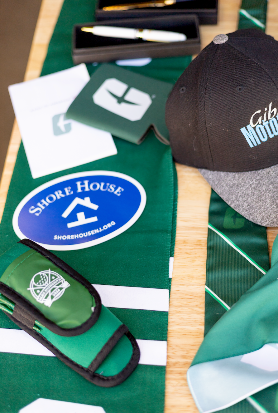 School supplies and accessories on a green table, including a Shore House sticker, lanyard, hat, and paper.
