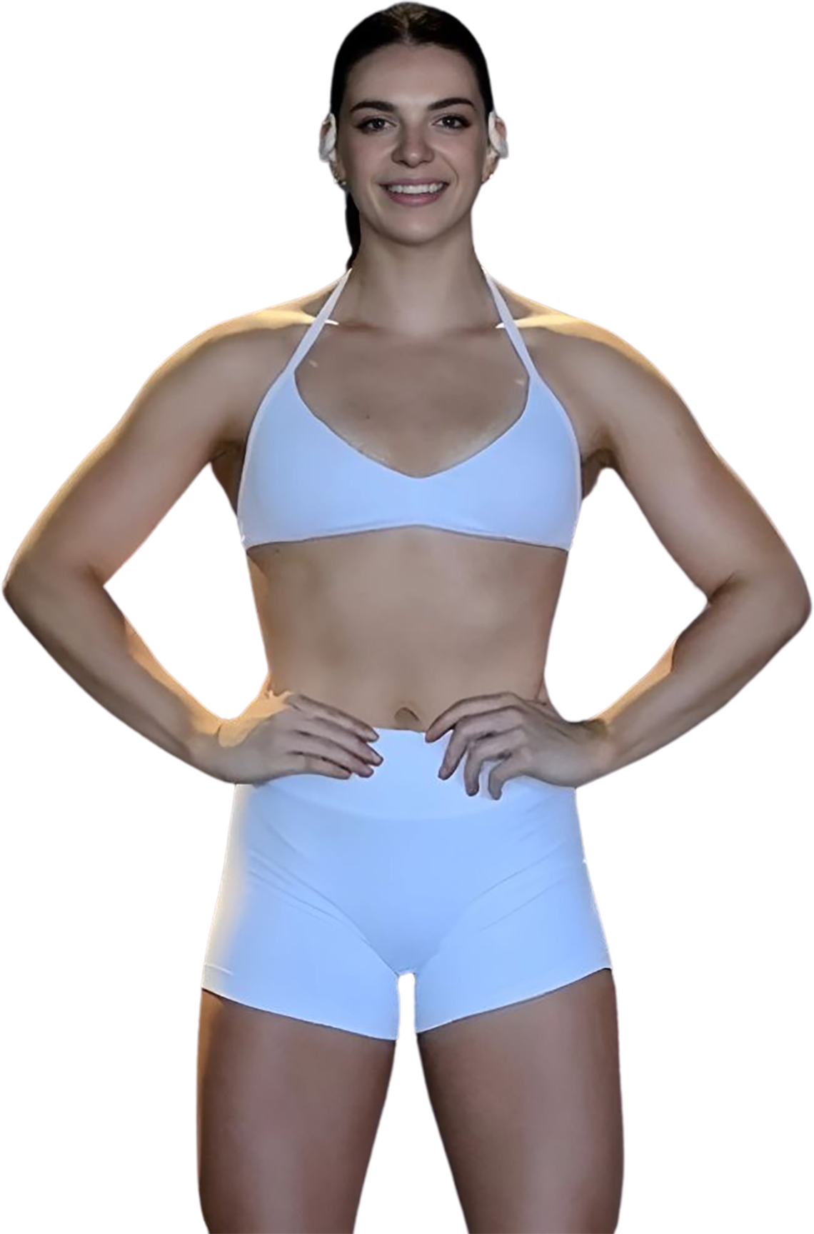 A woman in a white bikini top and shorts is standing with her hands on her hips.