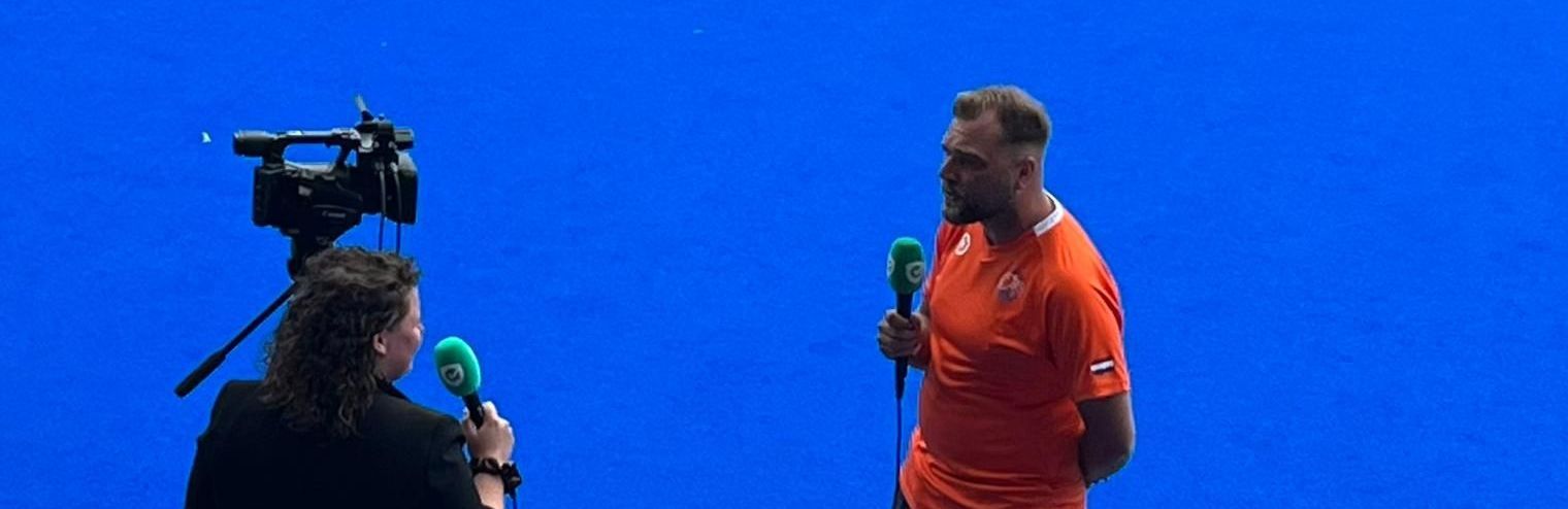 Een persoon in een oranje uniform wordt geïnterviewd voor een blauw scherm.