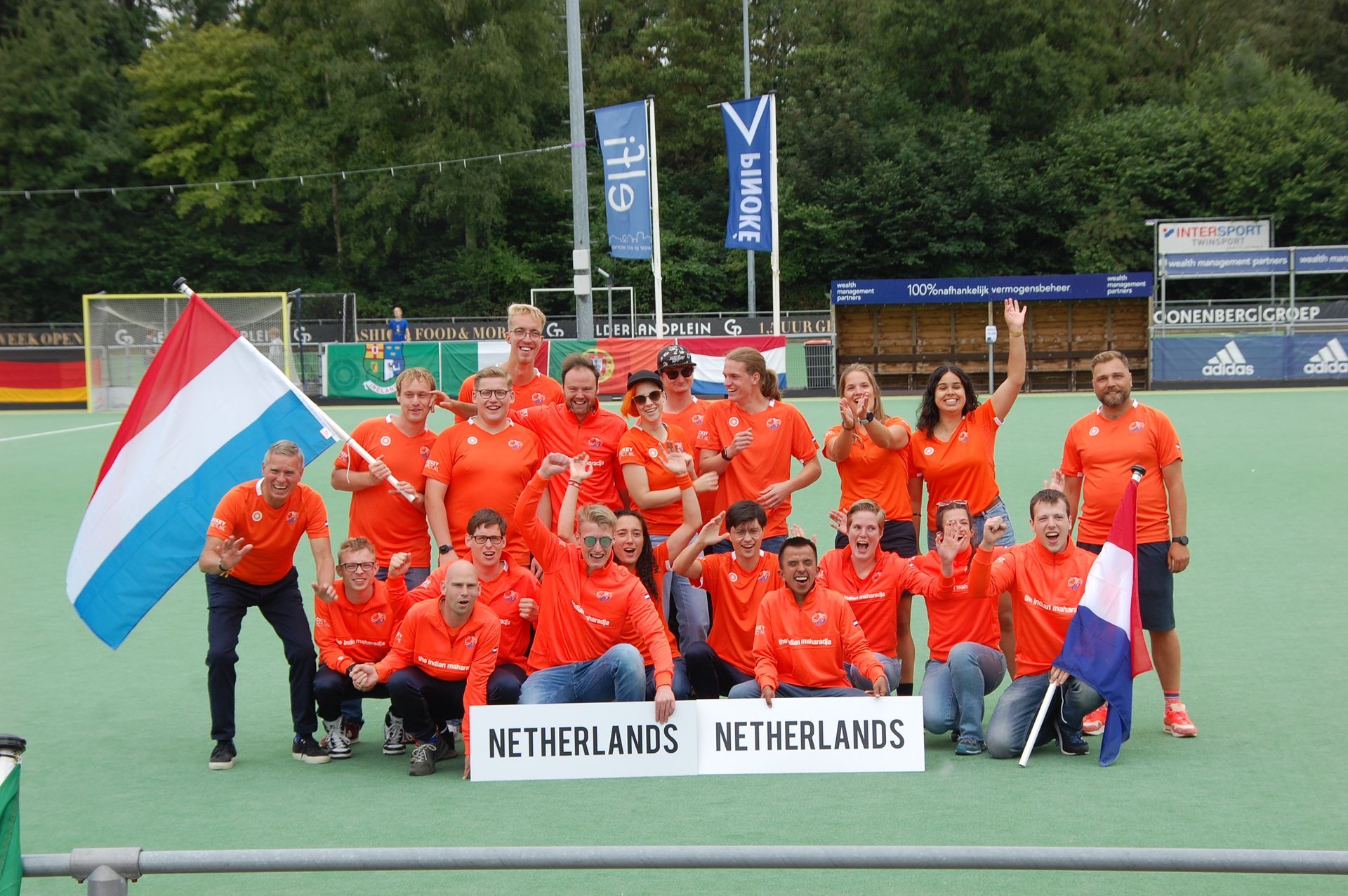 Het Nederlandse hockeyteam, in oranje tenue, viert de overwinning op het veld met de Nederlandse vlag en een bord met de tekst 