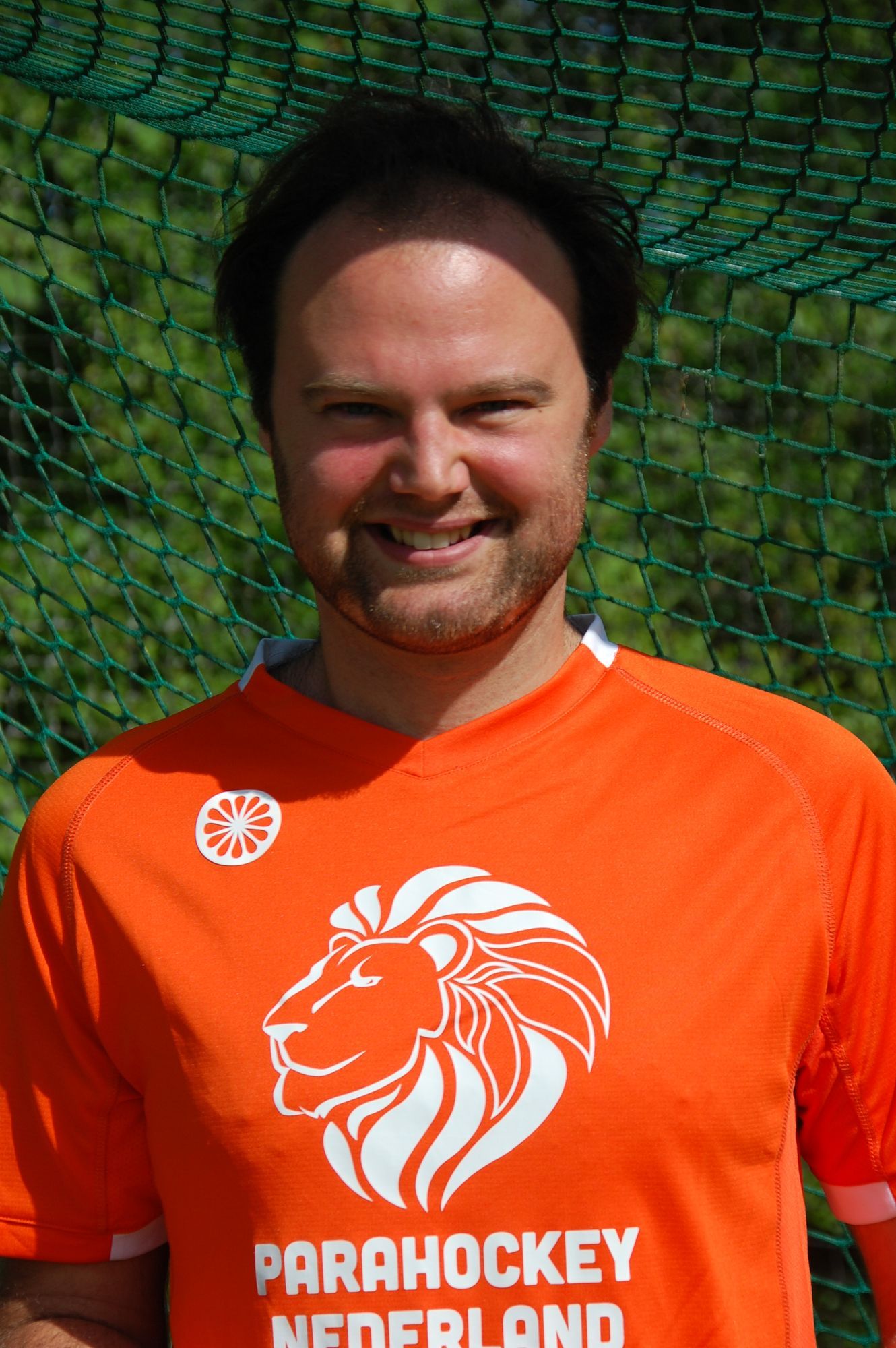 Man in oranje shirt met leeuwenlogo, lachend. Tekst 