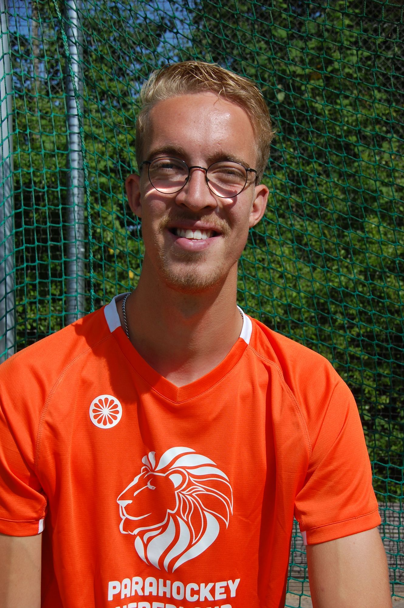 Man in oranje shirt met bril, lachend. Logo 