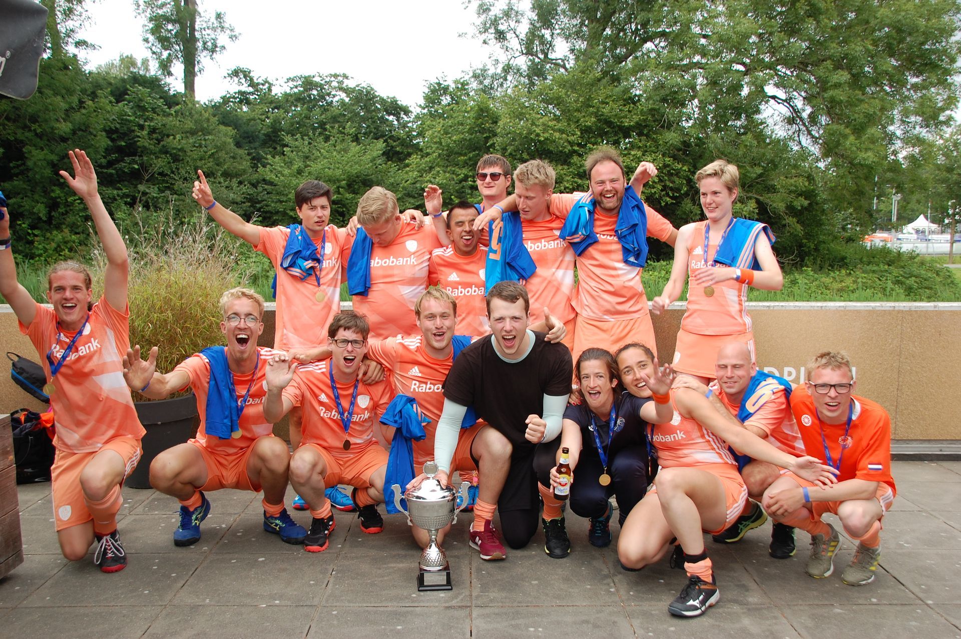 Het team in oranje uniformen viert de overwinning met de trofee in de buitenlucht.