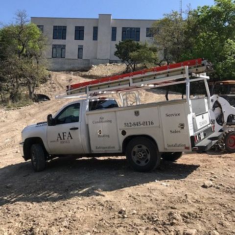 A white truck with a ladder on top of it is parked in a dirt field from AFA Service