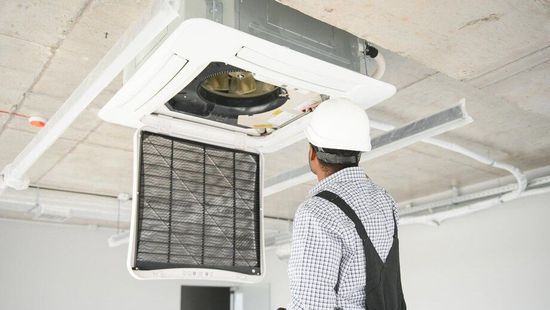 A man wearing a hard hat is working on an air conditioner.