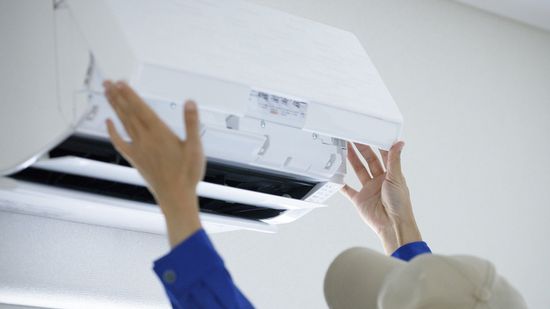 A person is fixing an air conditioner on the wall.