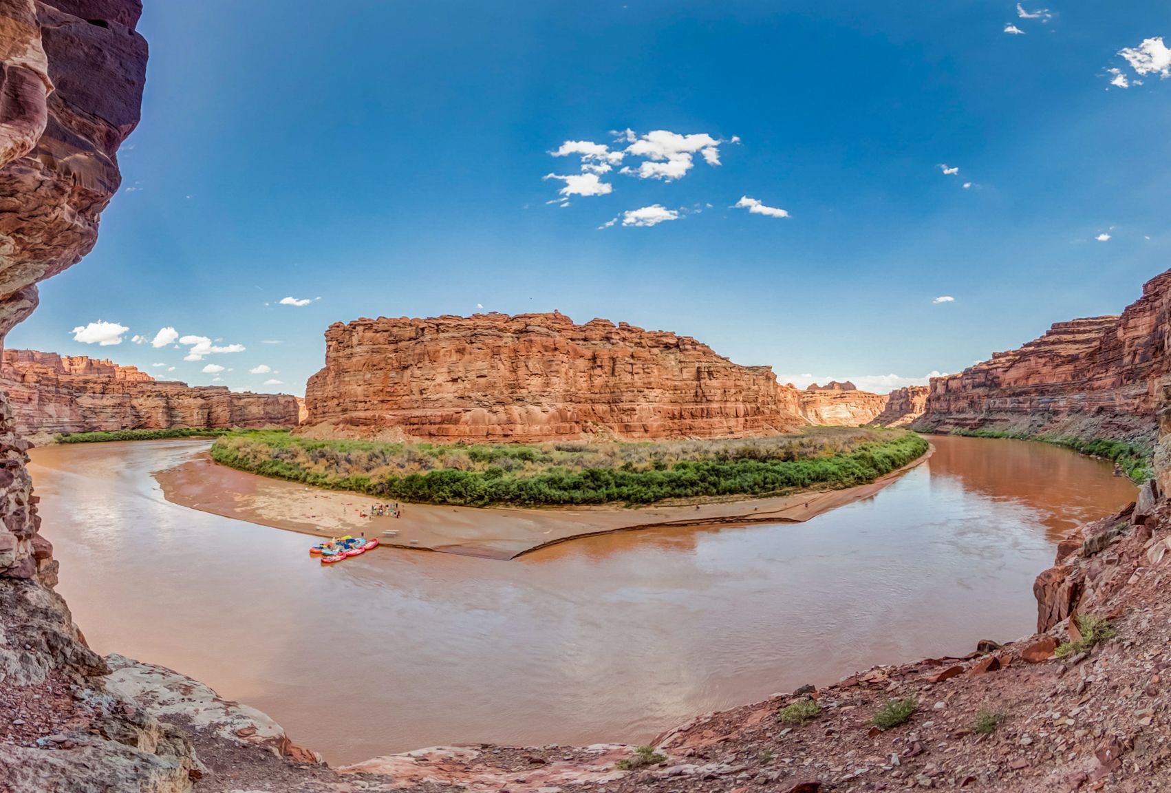 Colorado River winding around a massive plateau with rafts at a beach.
