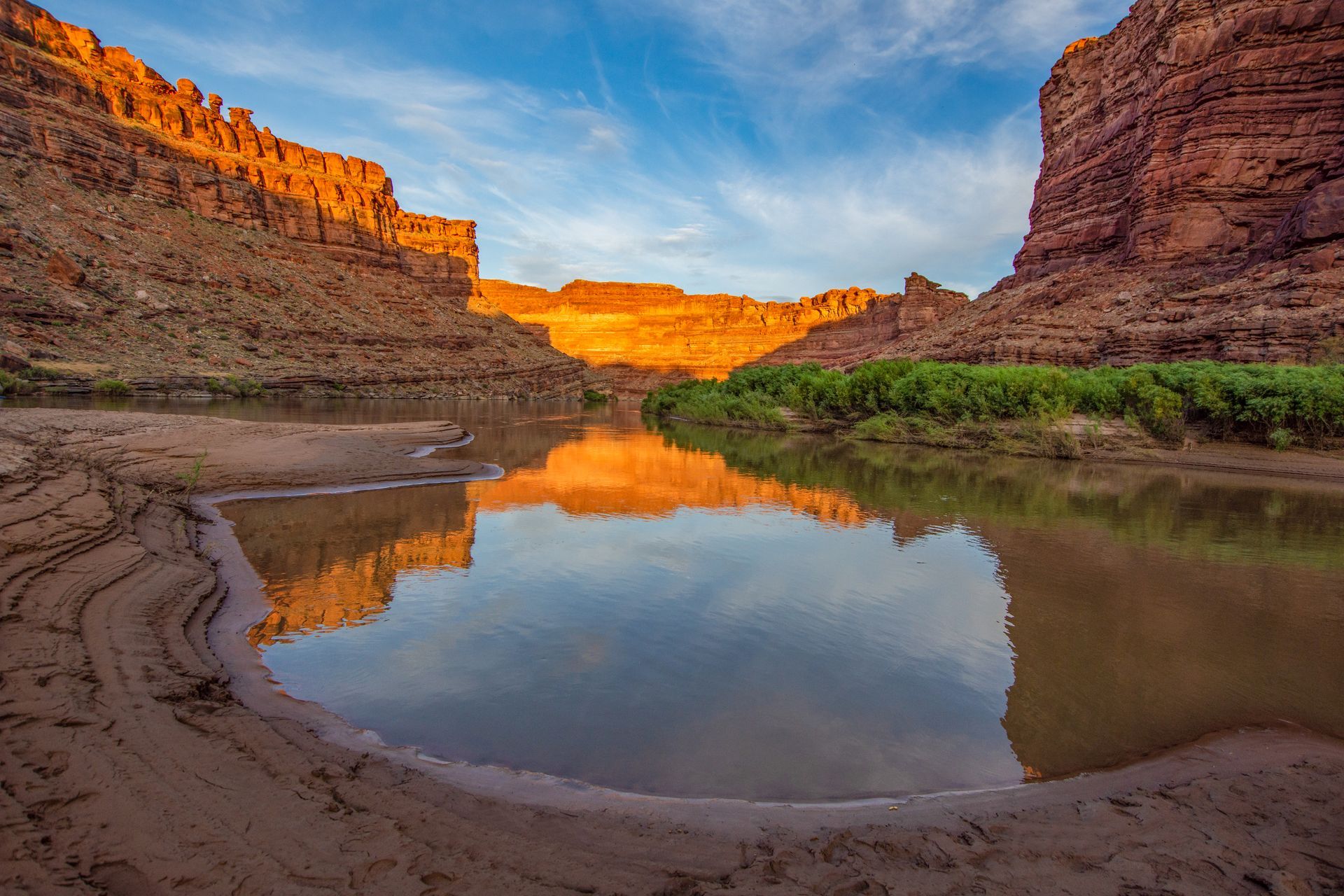 Boat on a river, passengers visible, against a backdrop of red rock cliffs at sunset.