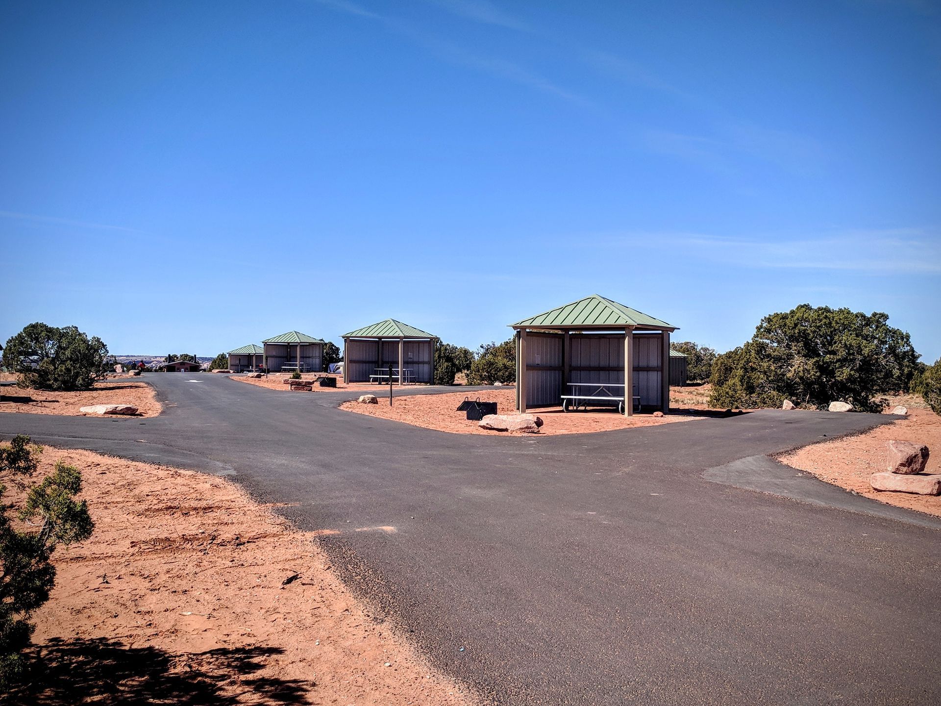 Campground road shows campsites with shaded pavillions covering picnic tables at each site.