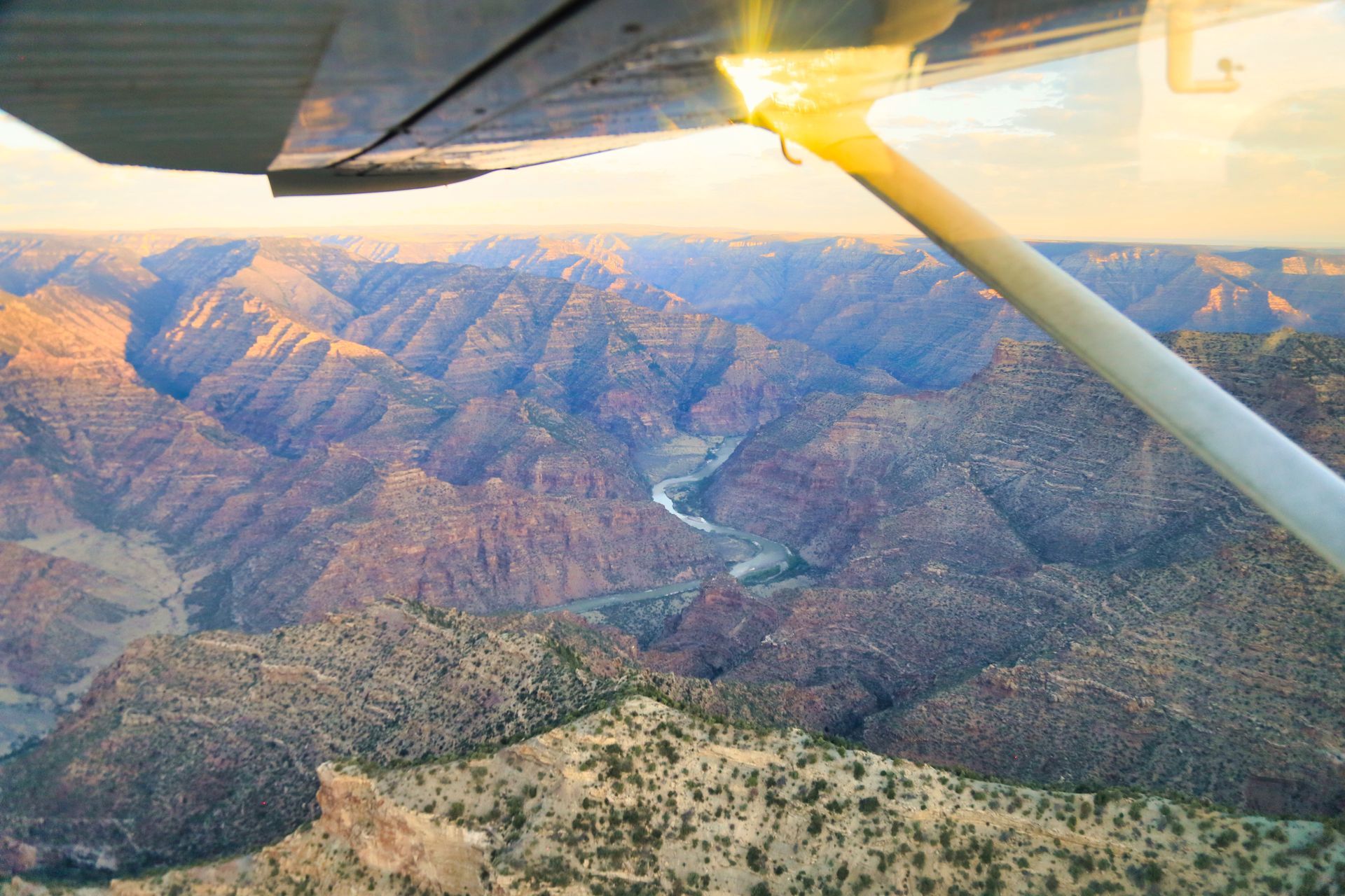 Boat on a river, passengers visible, against a backdrop of red rock cliffs at sunset.
