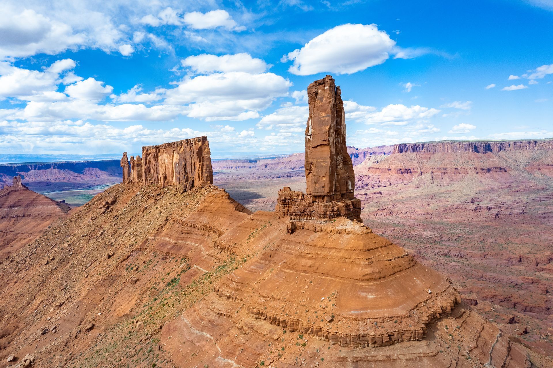 Castleton tower stands tall against a blue sky with buttes and canyons spanning into the horizon.