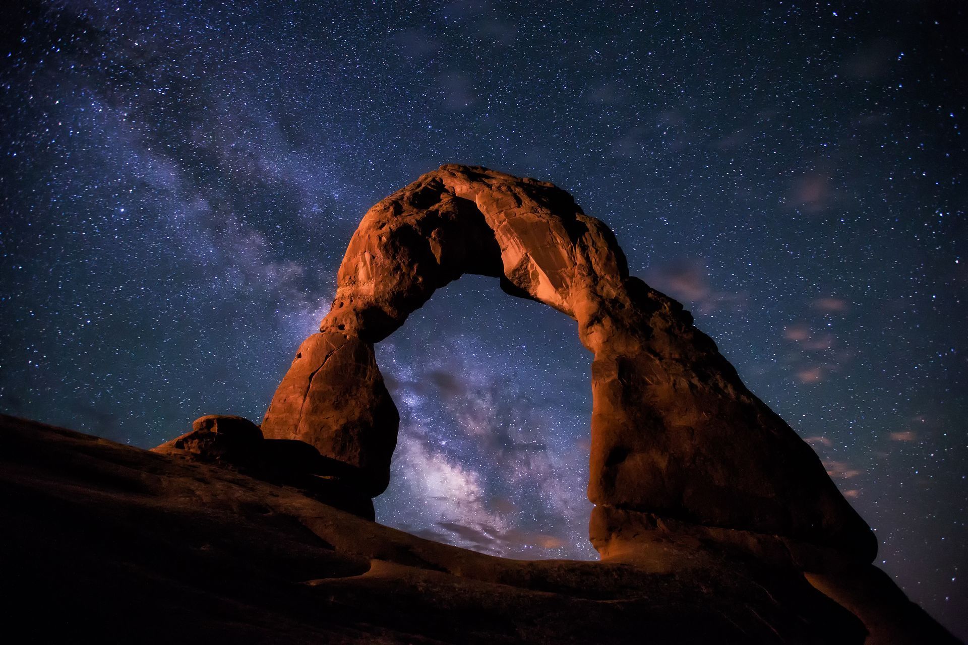 Delicate Arch under a starry night sky, Milky Way visible. Utah, orange rock formation.