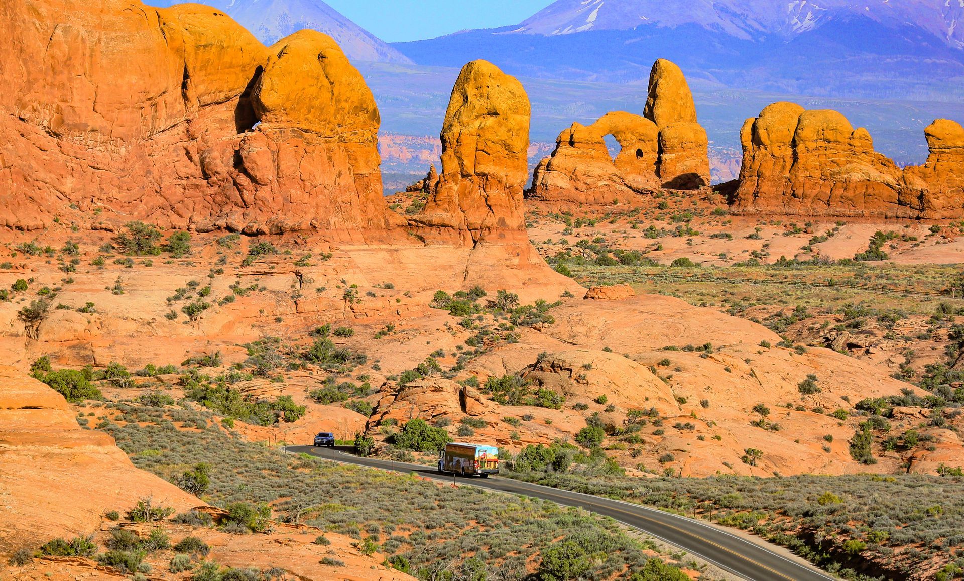 A tour bus drives along a road into the Windows section of Arches.