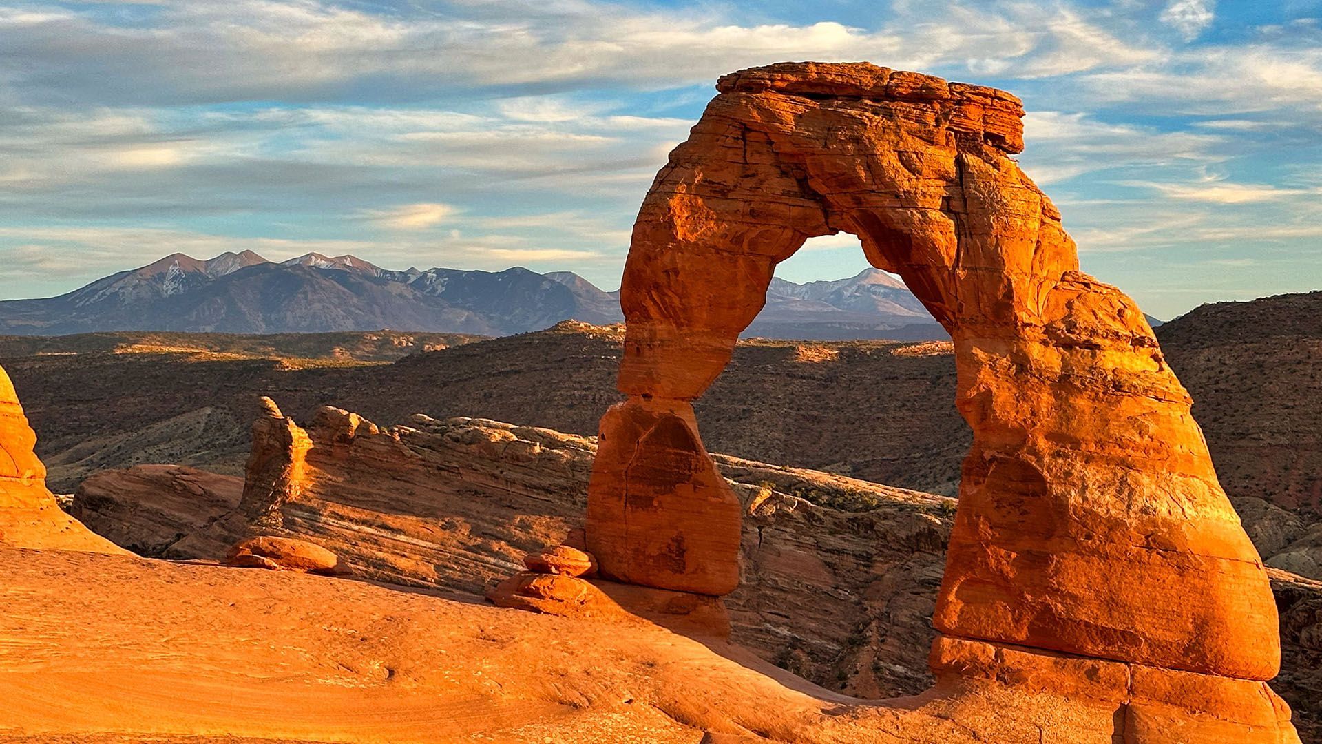 Delicate Arch in Arches National Park, Utah. Orange sandstone arch with mountains in the background at sunset.