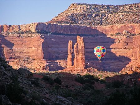 Hot air balloon floats between red rock formations in canyon.