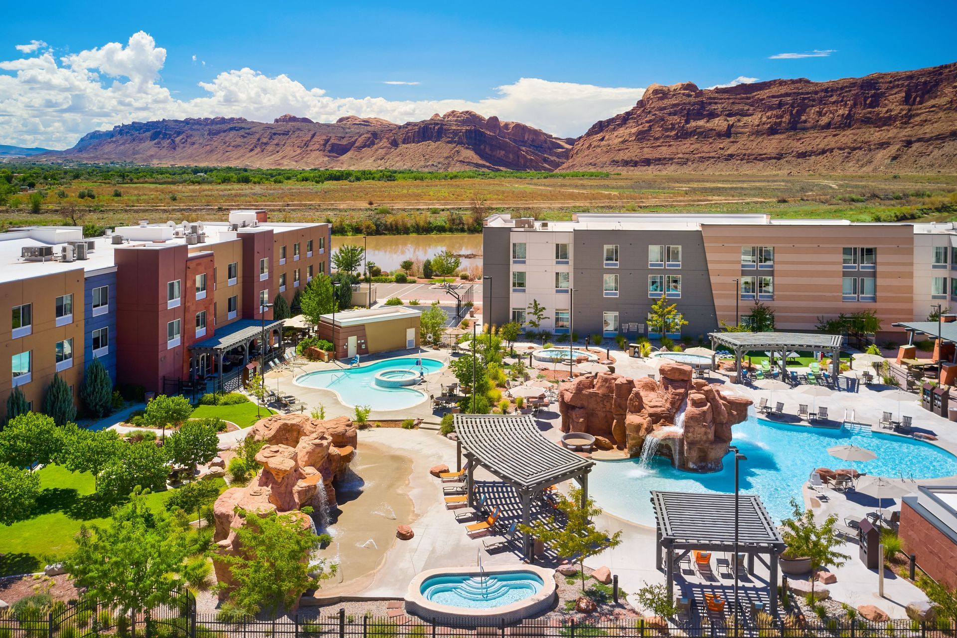 Hotel with pools, landscaping, and red rock mountains in the background. Blue sky, sunny day.