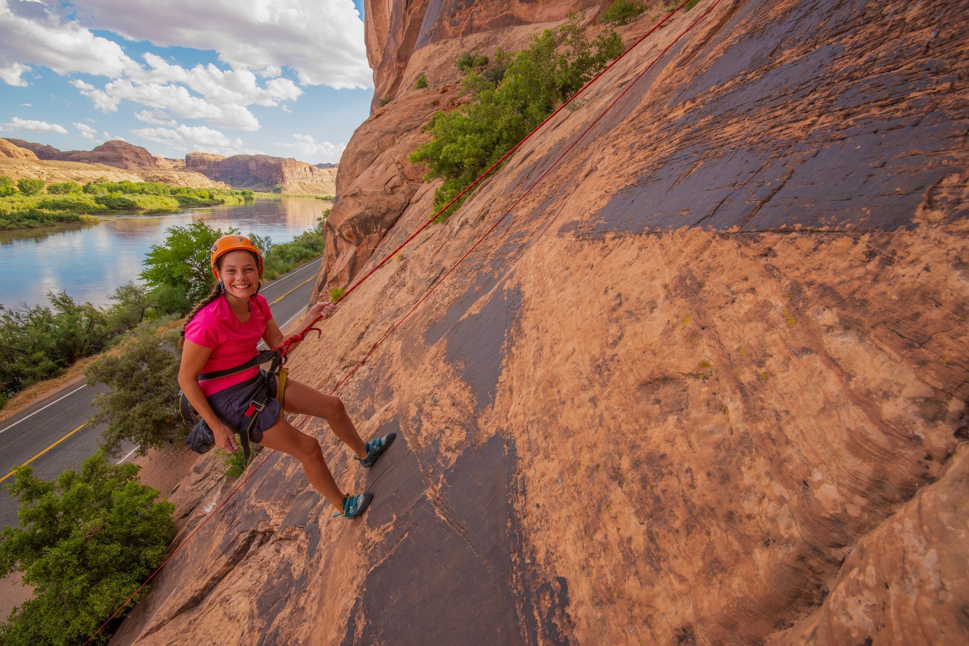 A woman is climbing a rock wall next to a river.