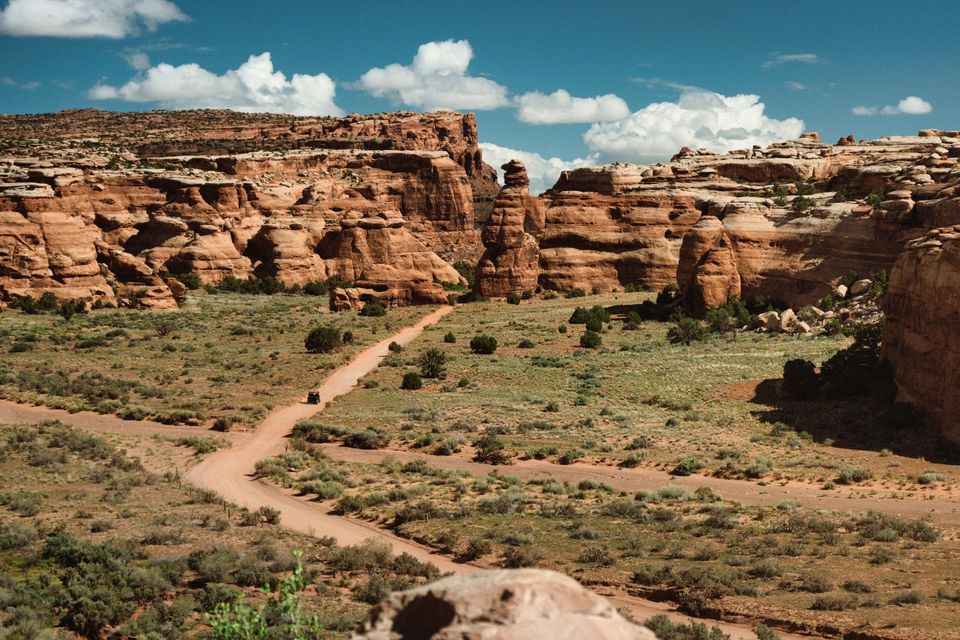 Dirt road betwen dramatic cliffs with blue sky and clouds behind. Vehicles driving on the road.