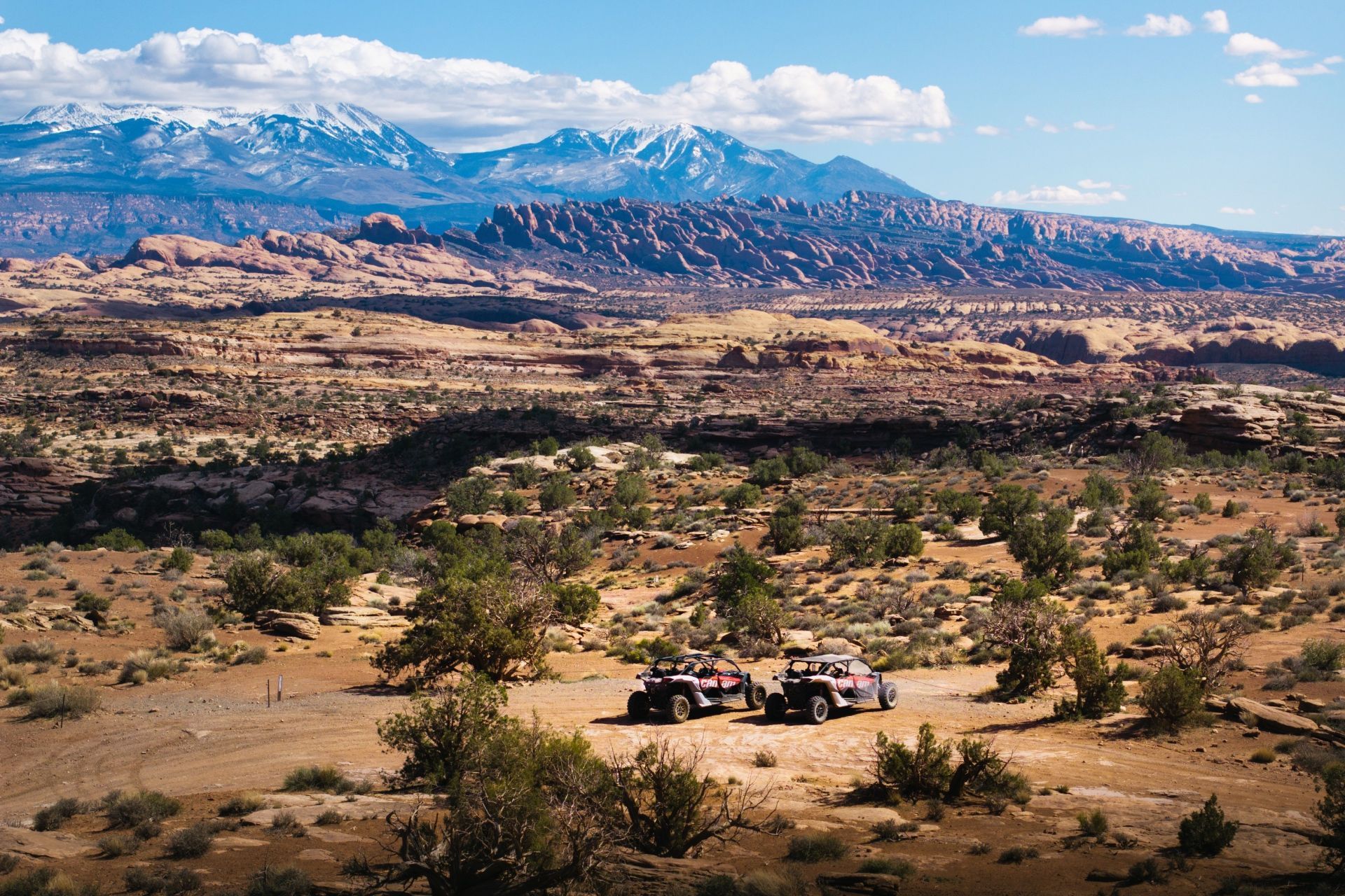 UTVs parked with a dramatic backdrop of red rock and the La Sal Mountains.