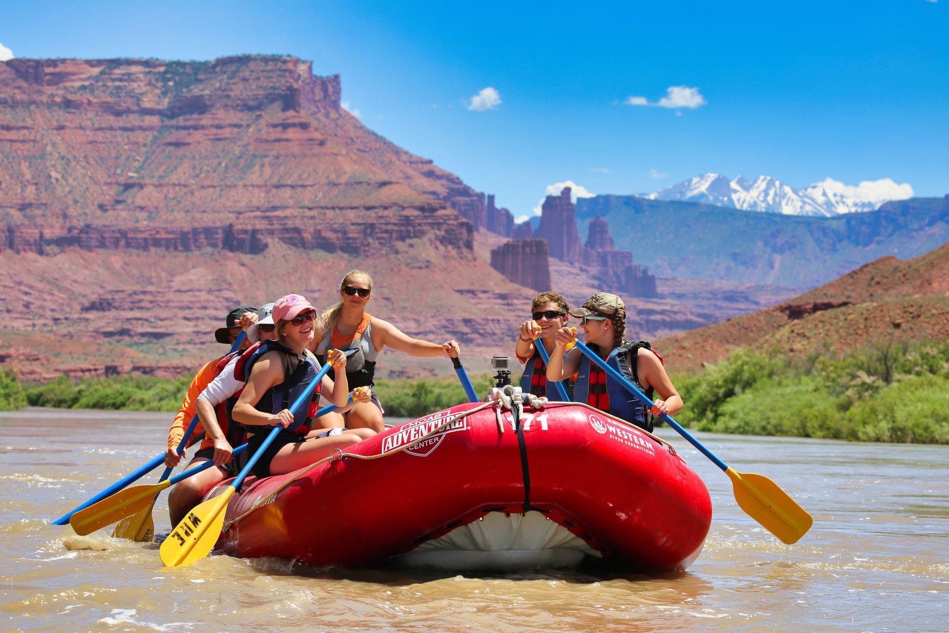 People rafting down a river in a red raft; red rock mountains in the background.