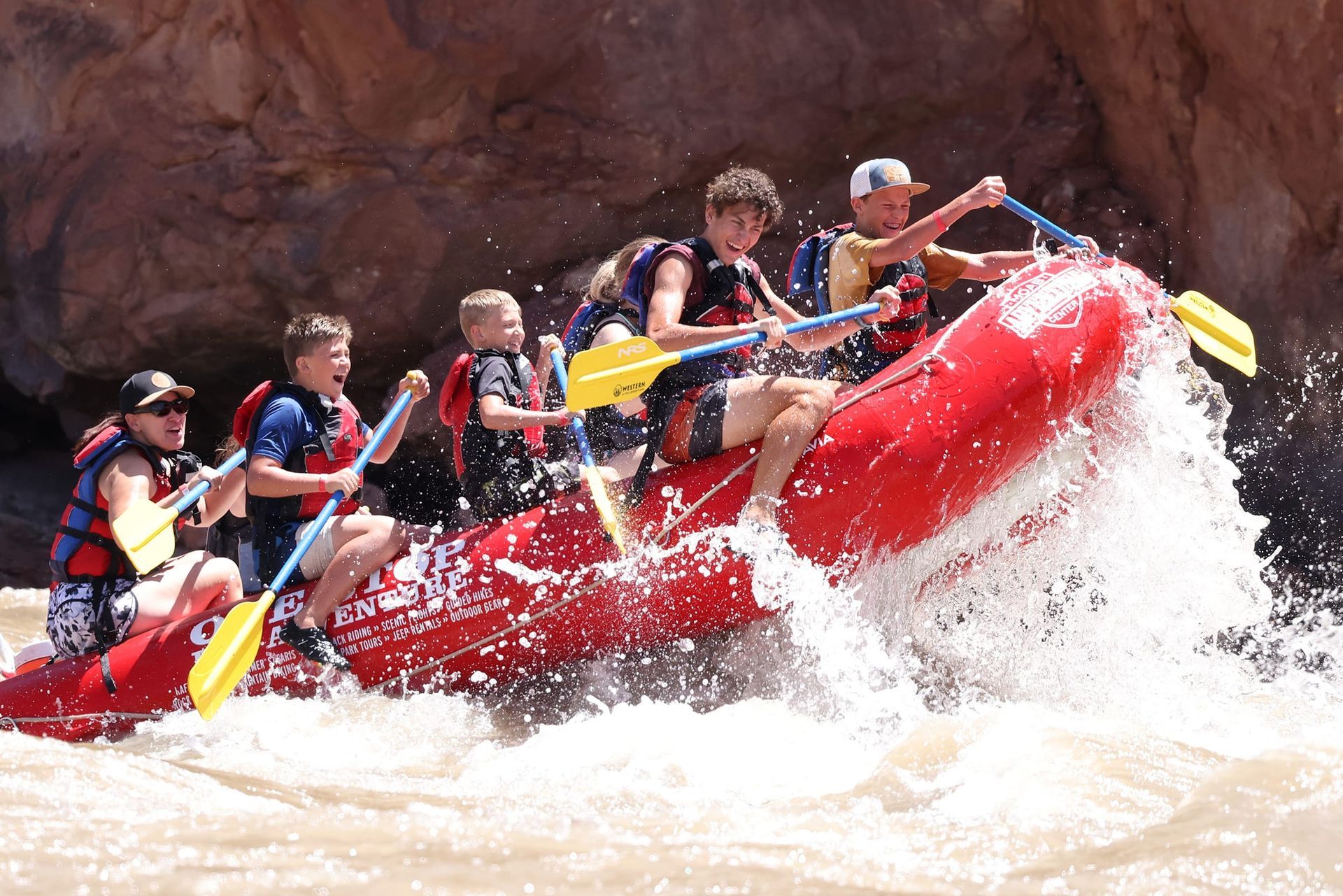 People white-water rafting in a red raft, paddling through rough water.
