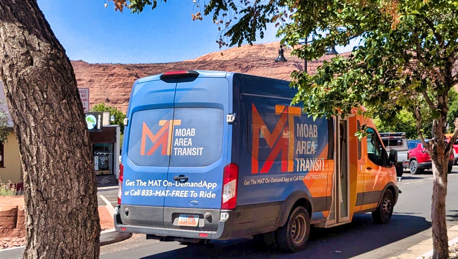 A blue and orange van with "Moab Area Transit" branding parked on a street, desert landscape in background.